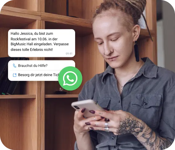 Eine junge Frau mit Tattoo schaut auf ihr Handy, um eine WhatsApp-Einladung zu einem Rockfestival zu sehen.